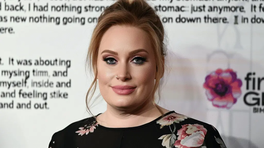 Adele posing on the red carpet in a sheer black dress with red floral embroidery during her weight loss journey transformation.